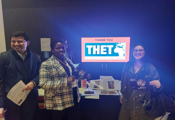 Three people gathered round a screen which has THET's logo on it, all smiling at the event.